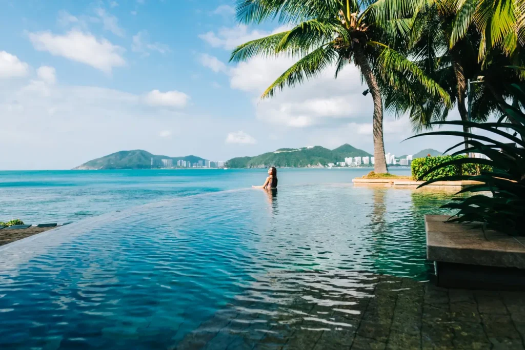 Junge Frau im Pool, blauer Himmel und Ozean im Hintergrund, Sommerurlaub, Pauschalreise